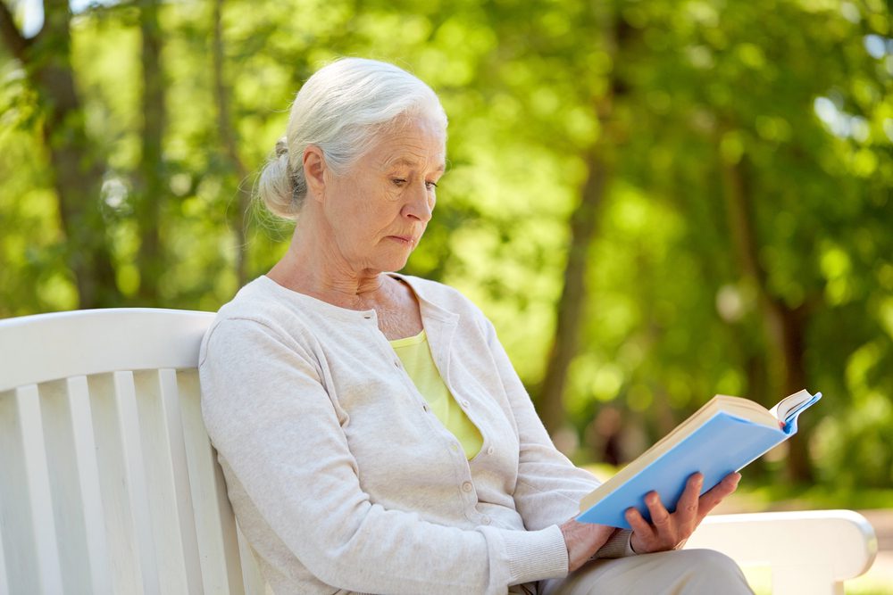 Beautiful woman reading a book on a bench. Things that matter less after fifty...concern over greying hair and wrinkles.